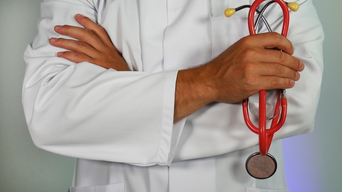 A clinician in a white coat holding a stethoscope with arms folded